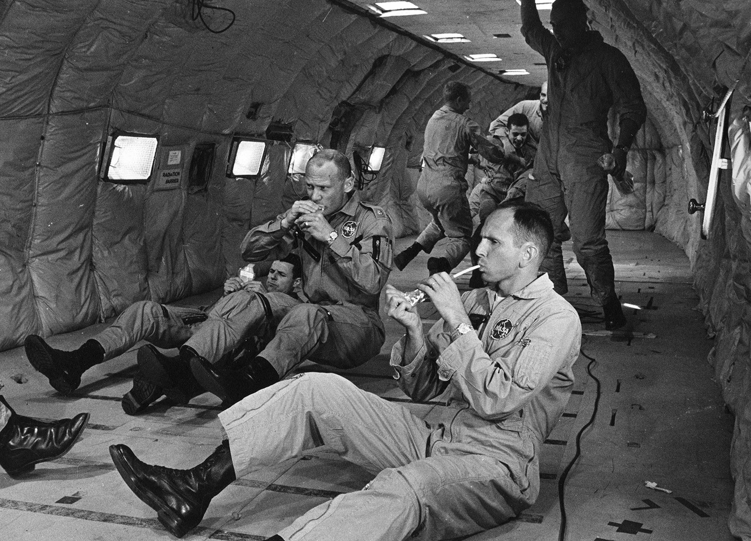 While flying parabolic arcs to simulate weightlessness aboard a KC-135 at Wright-Patterson AFB in August of 1964, Buzz Aldrin attempts to consume a container of space food. Fellow NASA astronauts Charlie Bassett (left) and Ted Freeman (right) are also trying to eat the specially prepared food. Credit: NASA via Retro Space Images