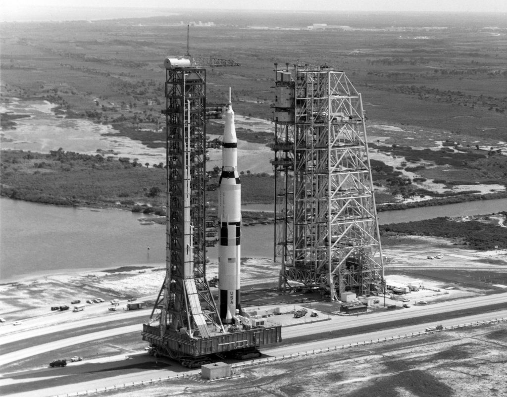 While traversing the 3.5 mile crawlerway to LC 39-A, the Saturn V passes the Mobile Service Structure, which will join it atop the pad as launch preps are continued.