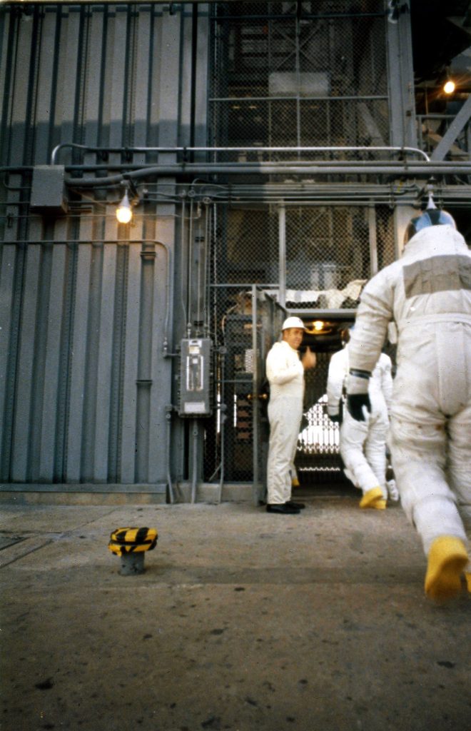 After having departed the transfer van at Pad 39A on launch morning, the crew prepares to board the first (ground level) elevator at the pad. They would soon transfer to a second elevator that would take them to the White Room at the 320 ft. level.