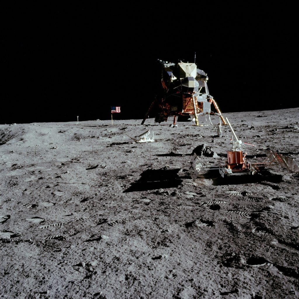 Resting on the lunar soil is a seismometer, part of the Early Apollo Scientific Experiments Package (EASEP). The Lunar Module and American flag can be seen in the distance.