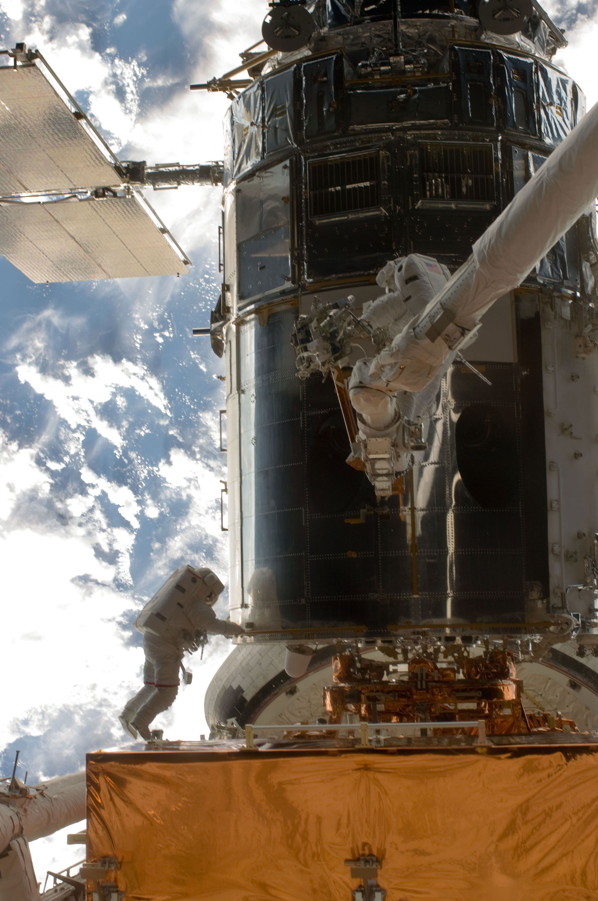 John Grunsfeld and Andrew Feustel, perched alone on the end of the Atlantis’ RMS arm, conduct the first of five STS-125 spacewalks to repair and upgrade the Hubble Space Telescope, temporarily locked down in the cargo bay of the Earth-orbiting shuttle. Credit: NASA