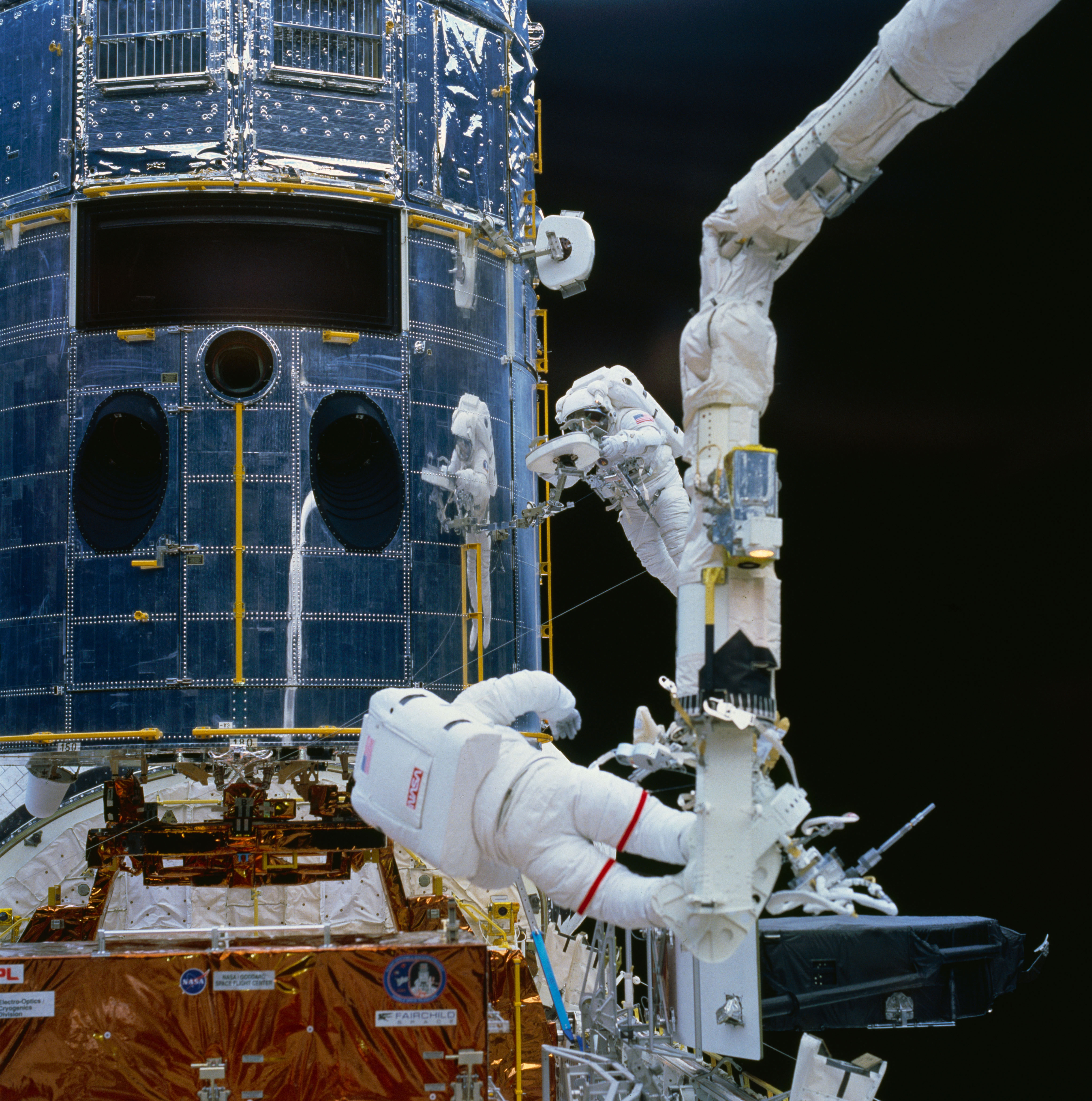 Astronaut Story Musgrave (top right center) works with a restraint device near the Hubble Space Telescope during the first of five STS-61 EVAs. Fellow NASA astronaut Jeffrey Hoffman is seen at the bottom of the frame preparing to work with fuse plugs. Credit: NASA