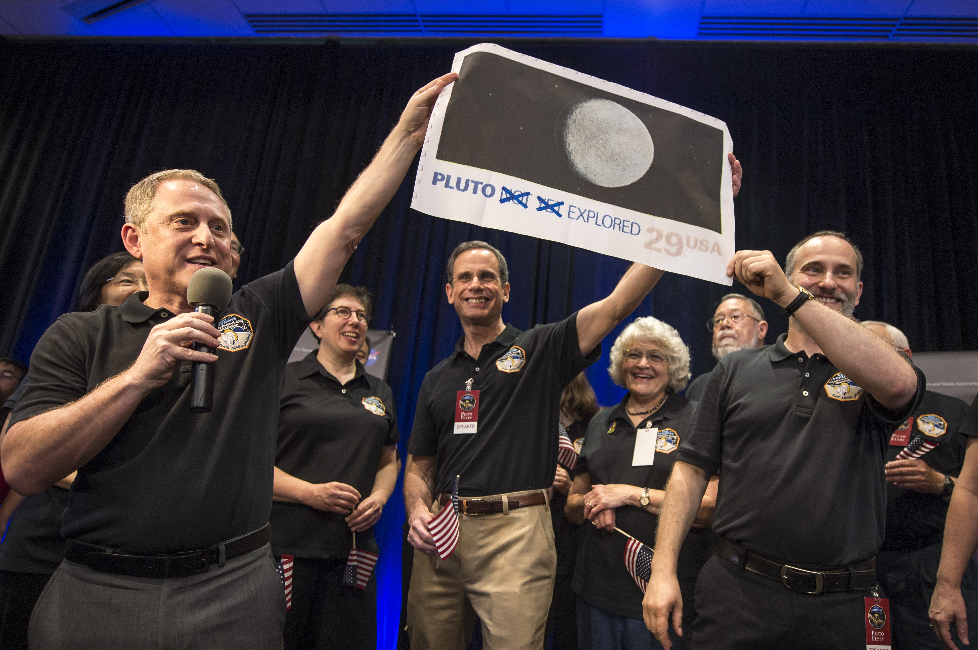 New Horizons Principal Investigator Alan Stern of Southwest Research Institute (SwRI), Boulder, CO., left, Johns Hopkins University Applied Physics Laboratory (APL) Director Ralph Semmel, center, and New Horizons Co-Investigator Will Grundy Lowell Observatory hold a print of an U.S. stamp with their suggested update since the New Horizons spacecraft has explored Pluto, Tuesday, July 14, 2015 at the Johns Hopkins University Applied Physics Laboratory (APL) in Laurel, Maryland. Credit: NASA/Bill Ingalls